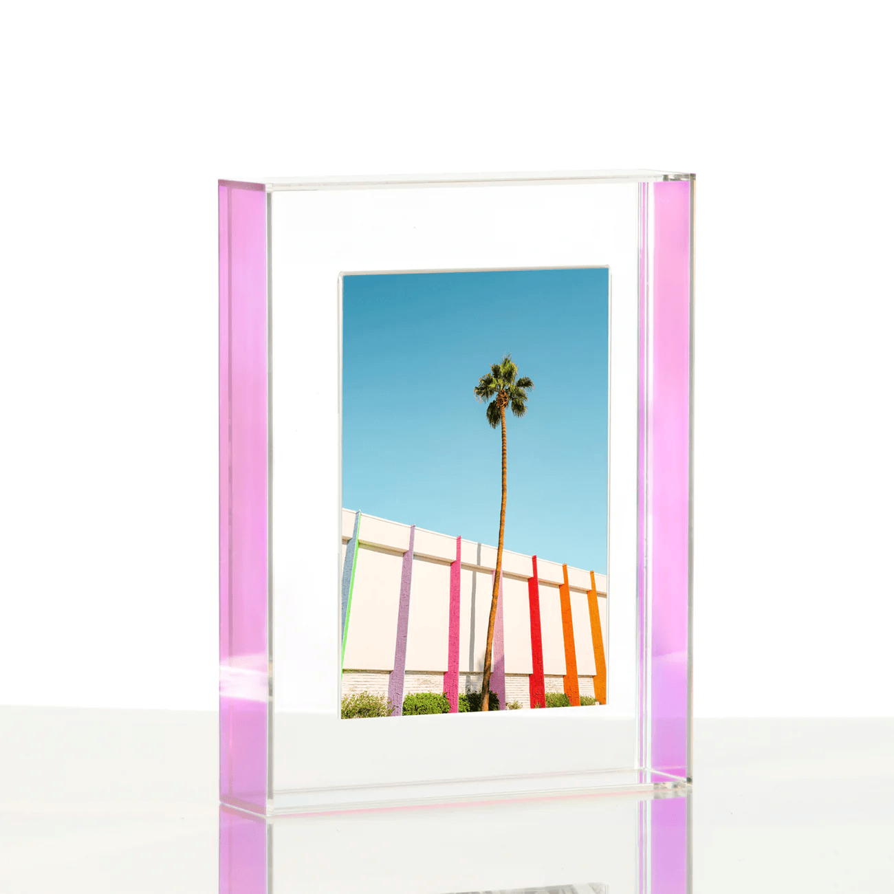A close up image of a clear block frame standing on a desk with a landscape photo inside it