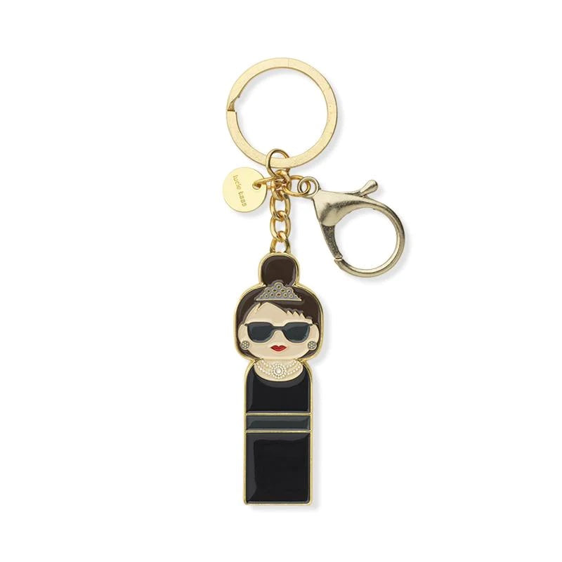 A gold keychain of a woman wearing red lipstick and sunglasses with a top bun