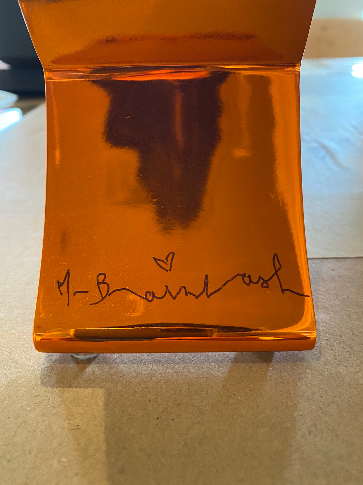 A reflective piece of orange metal with a signature on it