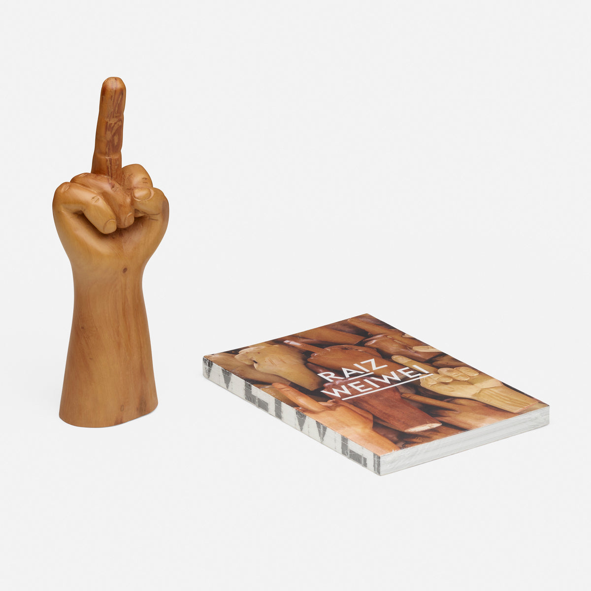 a sculpture of a gold hand with the middle finger pointed and a book next to it reading &quot;Raiz Weiwei&quot; 